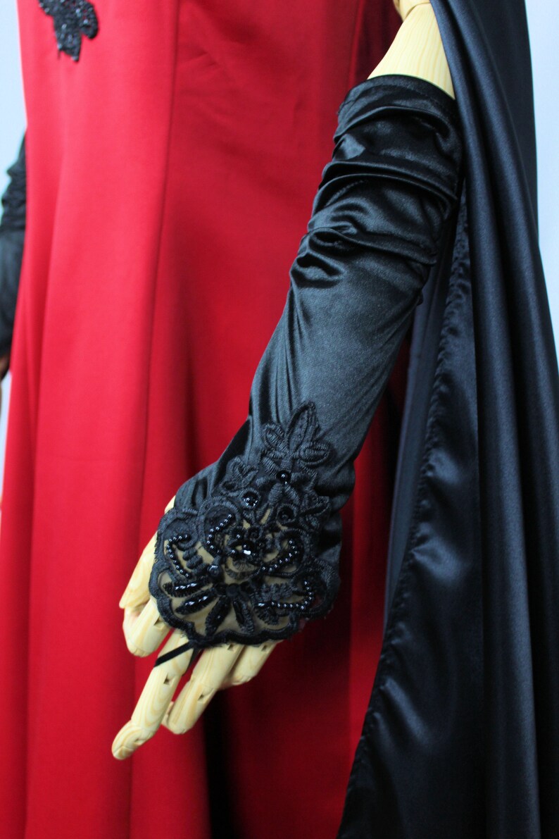 May include: A long black satin glove with a black lace and beaded trim. The glove is worn on a wooden hand.