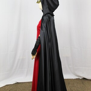May include: A black satin hooded cape with a long train. The cape is worn over a red dress.