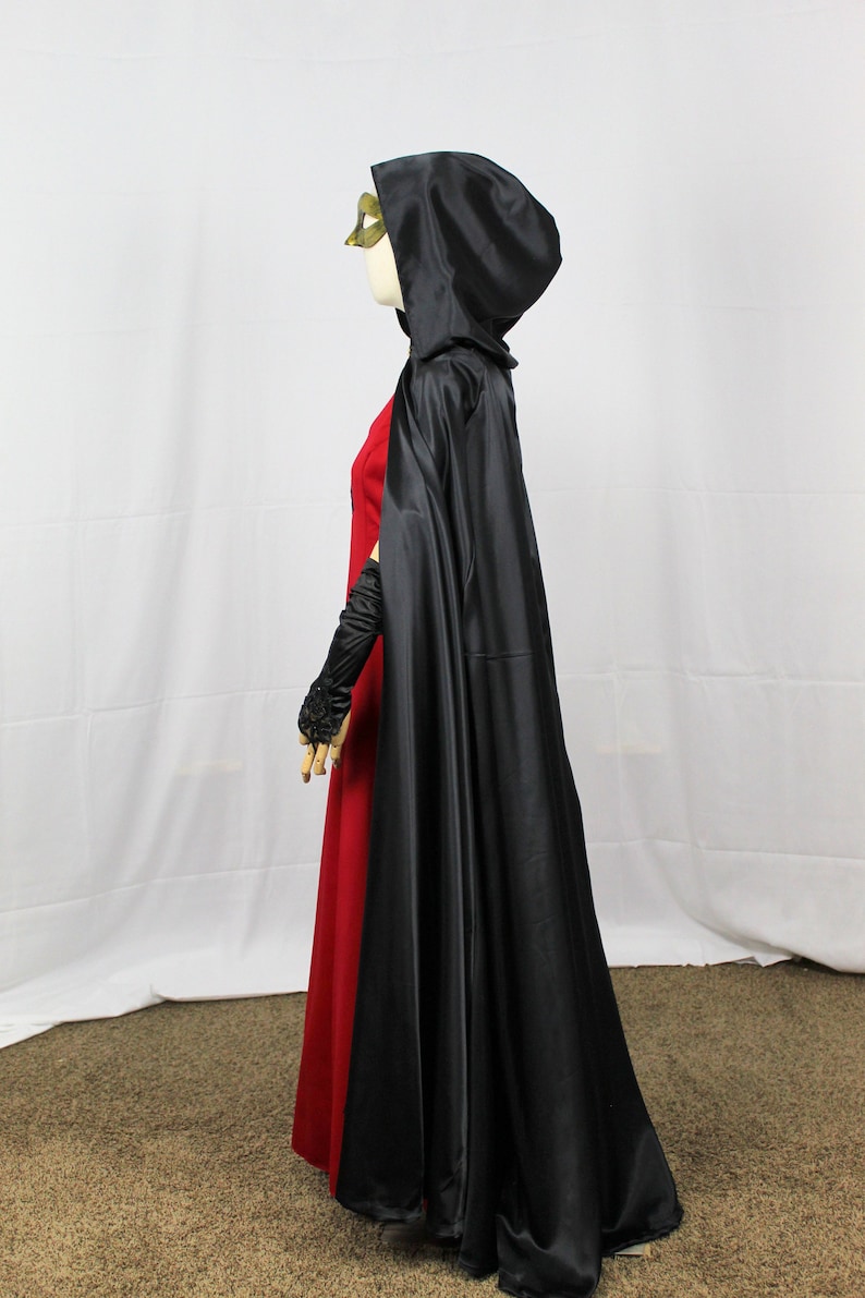 May include: A black satin hooded cape with a long train. The cape is worn over a red dress.
