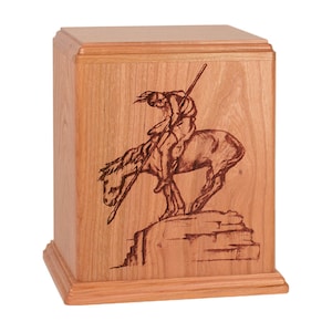 May include: A wooden cremation urn with a laser-engraved image of a Native American on horseback. The urn is a light brown color and has a simple design.