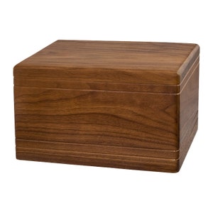 May include: A rectangular wooden box with a dark brown walnut finish. The box has a smooth, polished surface and a slightly rounded top.