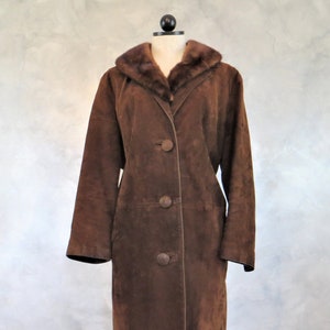 May include: A long brown suede coat with a fur collar. The coat has a button closure and a long, fitted silhouette.
