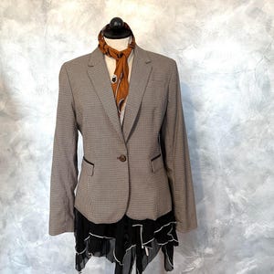 May include: A brown and white houndstooth blazer with a single-button closure and black trim. A patterned scarf in shades of brown and orange is draped over the blazer. A black and white layered skirt is visible beneath the blazer.