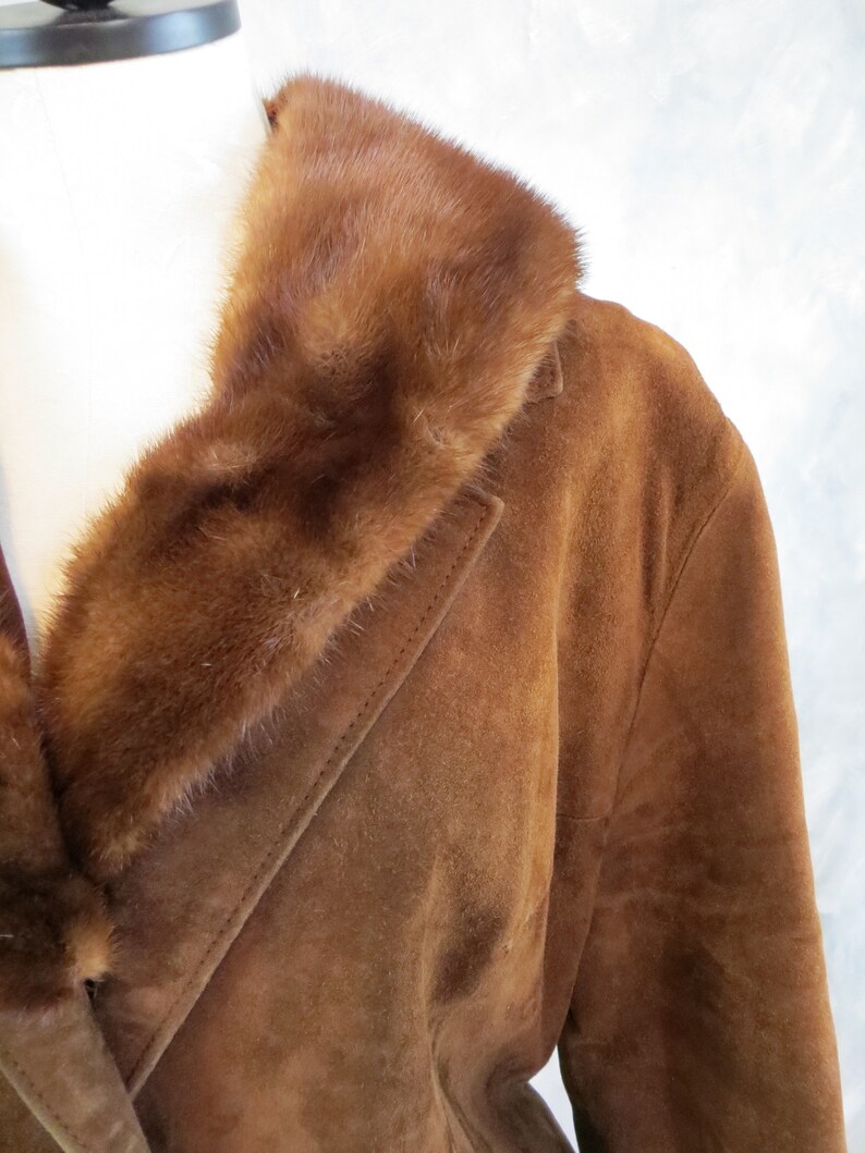 May include: A brown suede jacket with a brown fur collar. The jacket has a long sleeve and a button closure.