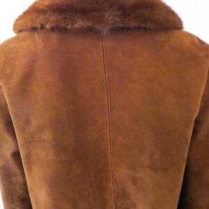 May include: A brown suede jacket with a brown fur collar. The jacket has a long sleeve and a classic design.