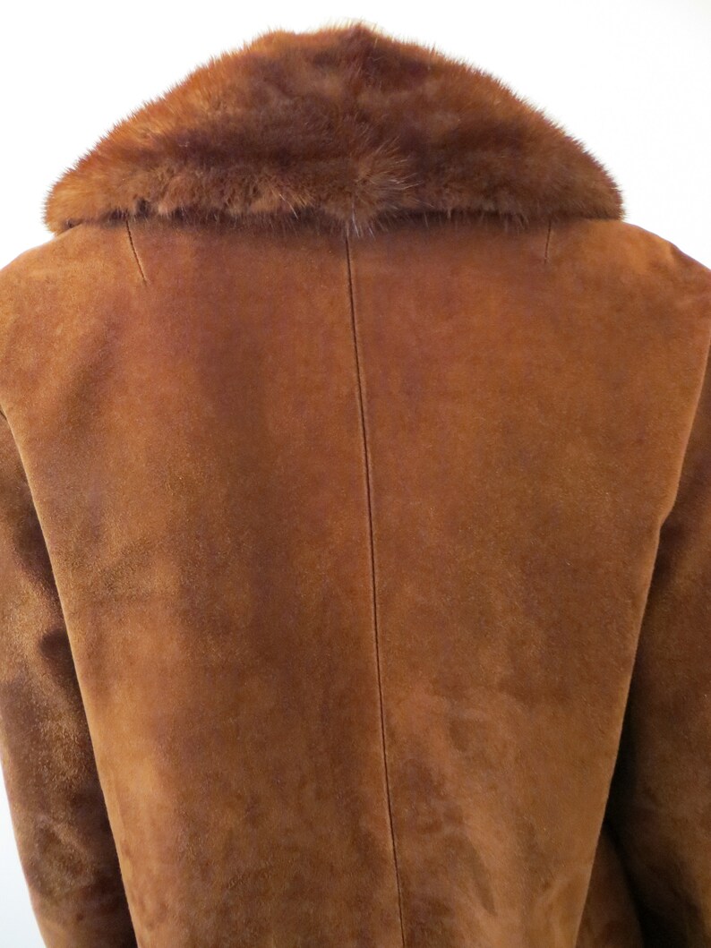 May include: A brown suede jacket with a brown fur collar. The jacket has a long sleeve and a classic design.