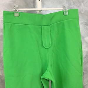 May include: A pair of bright green pants with a zipper detail on the front. The pants are made of a smooth, textured fabric.