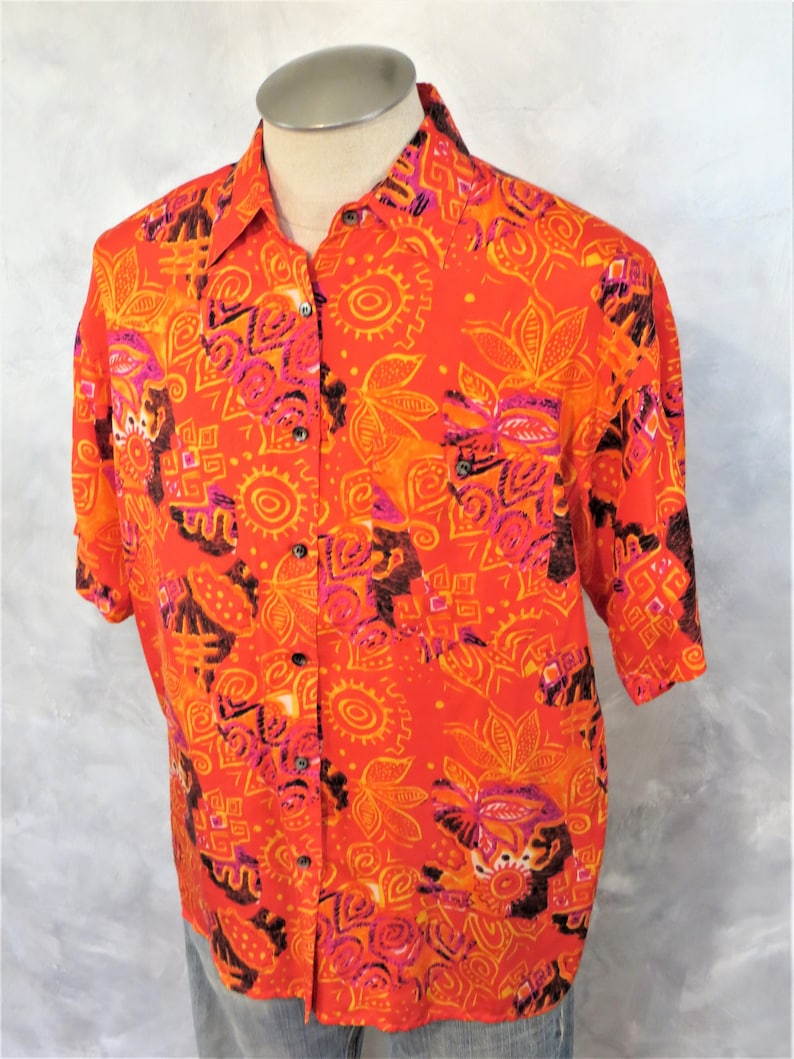 May include: A short-sleeved button-up shirt with a bright orange background and a colorful geometric pattern in shades of pink, orange, and brown.
