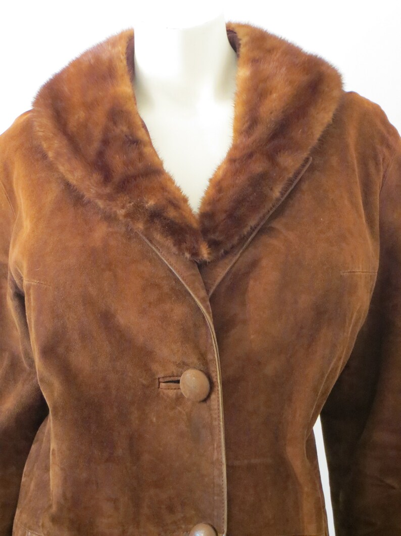 May include: A brown suede jacket with a fur collar. The jacket has a single button fastening and a v-neck.