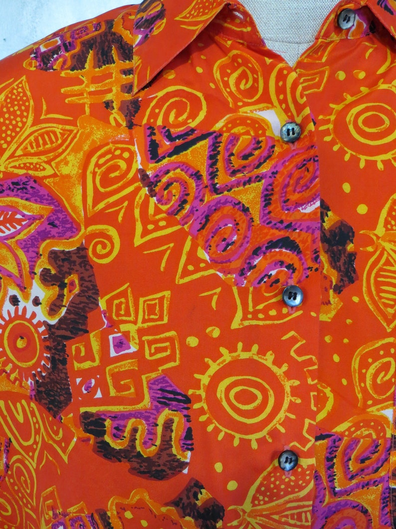 May include: Orange button-up shirt with a colorful abstract pattern featuring swirls, circles, and geometric shapes in shades of yellow, pink, and brown.