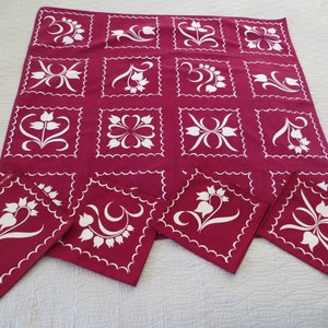 May include: A set of red and white floral table linens. The tablecloth features a repeating pattern of white stylized flowers on a burgundy background. The napkins are the same design as the tablecloth.