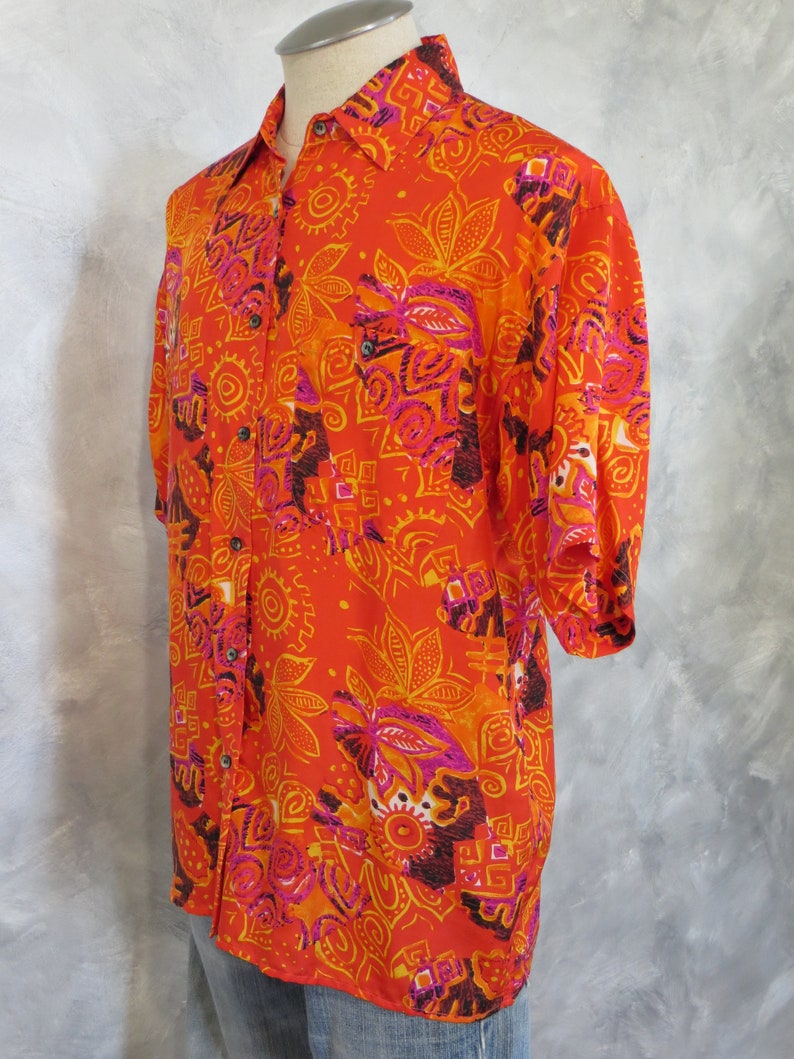 May include: A short-sleeved button-down shirt with a vibrant orange, pink, and yellow patterned design. The pattern features geometric shapes and floral motifs.
