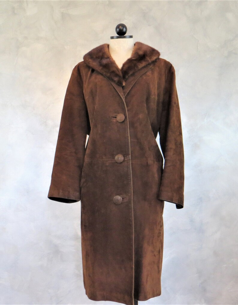 May include: A long brown suede coat with a fur collar. The coat has a button closure and a long, fitted silhouette.