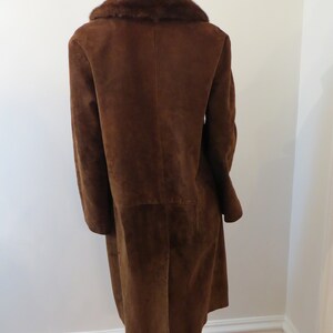 May include: A long brown suede coat with a fur collar. The coat has a single-breasted closure and long sleeves.