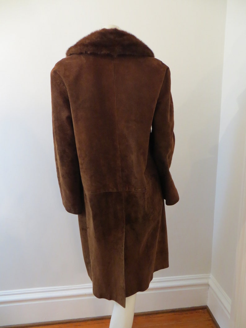 May include: A long brown suede coat with a fur collar. The coat has a single-breasted closure and long sleeves.