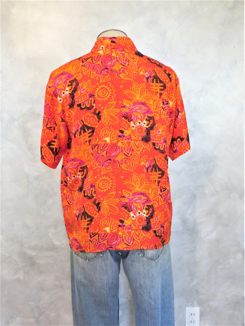 May include: A short-sleeved button-up shirt with a bright orange background and a colorful abstract pattern. The pattern features pink, orange, and black geometric shapes and designs.