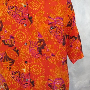 May include: A short-sleeved button-down shirt with a vibrant orange, yellow, and pink geometric pattern. The shirt has a collar and a pocket on the left side.