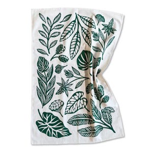 May include: White kitchen towel with a dark green botanical leaf pattern. The design features various leaf shapes and floral elements, creating a natural and decorative aesthetic. The towel is folded, showing the printed design.