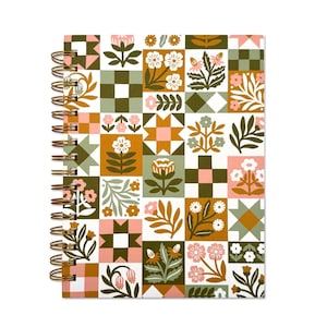 May include: A spiral-bound notebook with a colorful patchwork design. The cover features a repeating pattern of floral and geometric blocks in shades of pink, green, brown, and white. The spiral binding is gold-colored.