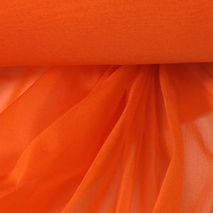 May include: Vibrant orange 100% silk organza fabric. The fabric is rolled up, with a portion draped down, showcasing its sheer texture. The text "Lee & Pearl" is in the upper left corner, and "Vibrant Orange" is in the lower right.