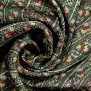 May include: Gray green silk twill fabric with a geometric pattern of red and yellow squares. The fabric is folded and twisted, showing the texture and pattern. #215 Gray Green Deco Geometric 100% Silk Twill