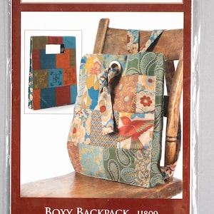 May include: A patchwork fabric backpack with a red bird design. The backpack has a drawstring closure and a flap with a buckle. The backpack is sitting on a wooden chair. The pattern is called "Boxy Backpack IJ809".