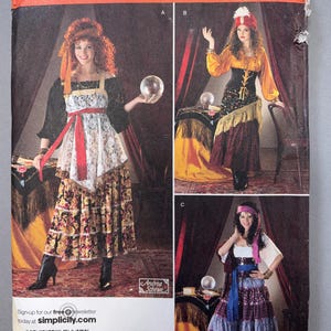May include: A Simplicity sewing pattern envelope 2331 for costumes in sizes 14, 16, 18, 20, 22. The front displays three variations of a multi-layered skirt and blouse outfit with accessories like headscarves, a red sash, and a crystal ball prop.