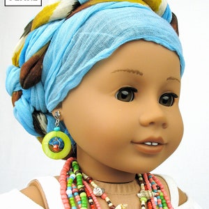 May include: A doll wearing a blue and brown patterned headscarf, a white top, and a multi-colored beaded necklace. The doll is wearing green and red earrings with a wooden circle.