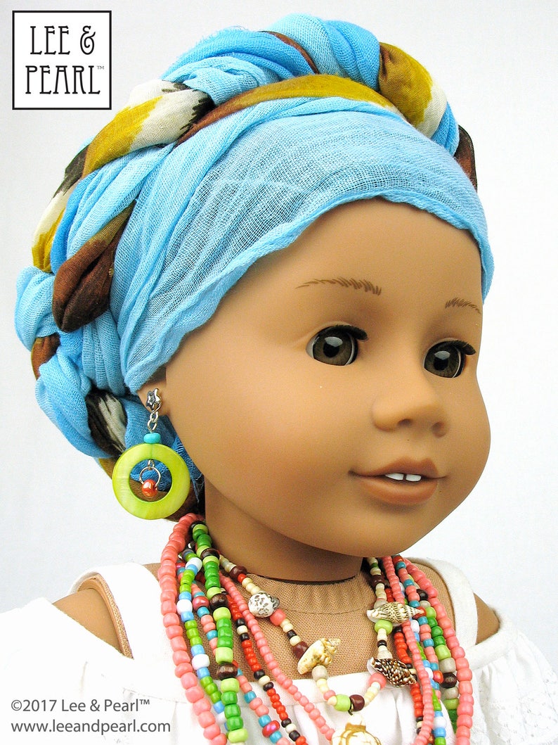 May include: A doll wearing a blue and brown patterned headscarf, a white top, and a multi-colored beaded necklace. The doll is wearing green and red earrings with a wooden circle.