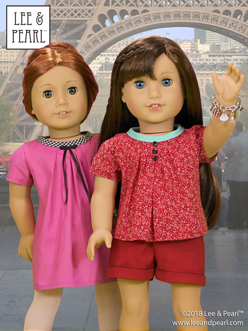 May include: Two dolls wearing different outfits stand in front of the Eiffel Tower. The doll on the left is wearing a pink dress with a black bow. The doll on the right is wearing a red and white patterned shirt with red shorts. She is also wearing a charm bracelet on her wrist.