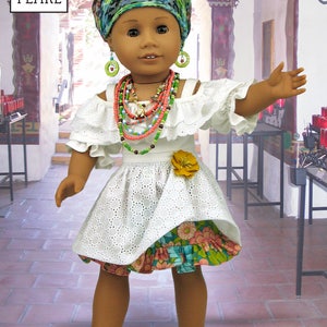May include: A doll wearing a white dress with a floral print skirt, a green and blue patterned head wrap, and multiple necklaces. The doll is standing in a room with a tiled floor and a doorway in the background. The doll is wearing blue sandals.