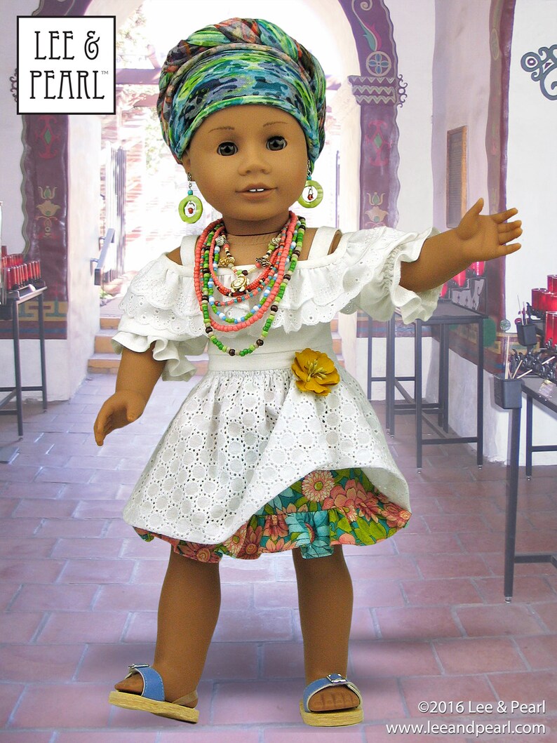 May include: A doll wearing a white dress with a floral print skirt, a green and blue patterned head wrap, and multiple necklaces. The doll is standing in a room with a tiled floor and a doorway in the background. The doll is wearing blue sandals.