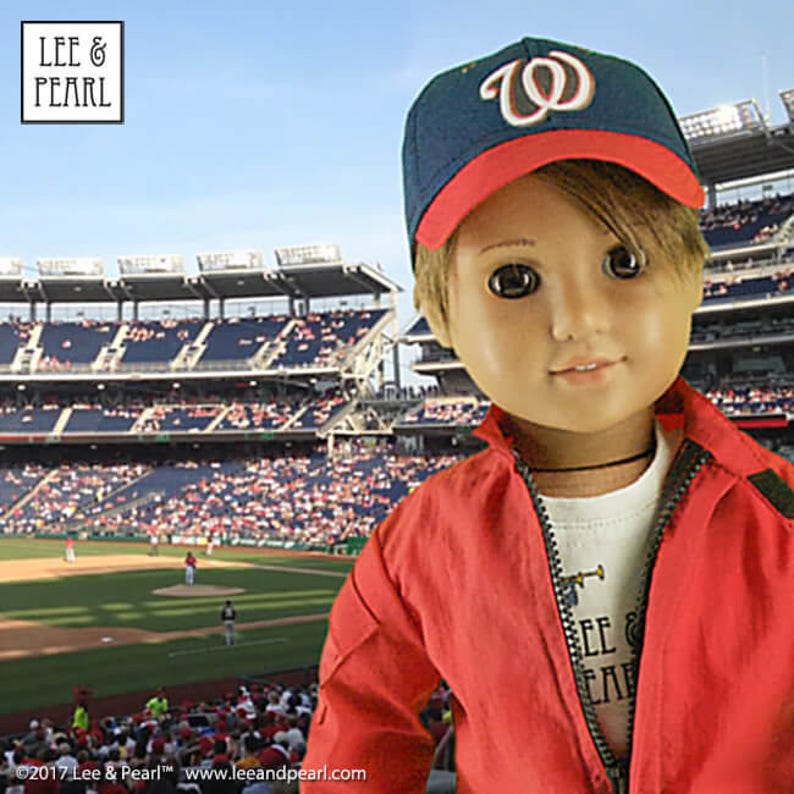 Peut inclure: Une poup&eacute;e portant une veste rouge, une chemise blanche et une casquette de baseball bleue et rouge avec un "W" blanc sur le devant. La poup&eacute;e est debout devant un stade de baseball.
