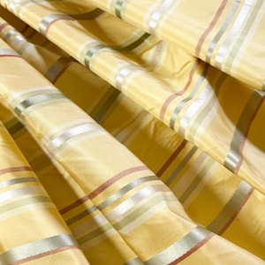 May include: A yellow fabric curtain featuring a repeating striped pattern. The design consists of horizontal bands in shades of light green, white, and muted orange, set against a bright yellow background with a subtle sheen and soft folds.