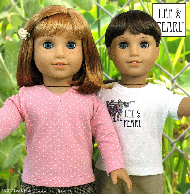 May include: Two dolls wearing pink and white polka dot and white shirts with the text "Lee & Pearl" on them. The dolls are standing in front of a green leafy background.