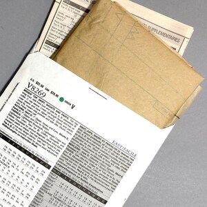May include: A sewing pattern packet with a tan envelope peeking out from a white and green printed instruction sheet. The packet includes measurements and instructions for a top, skirt, shorts, and pants.
