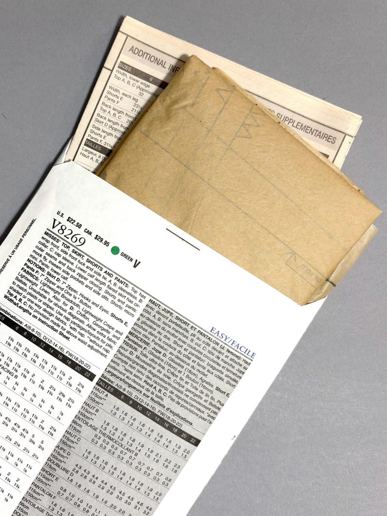 May include: A sewing pattern packet with a tan envelope peeking out from a white and green printed instruction sheet. The packet includes measurements and instructions for a top, skirt, shorts, and pants.