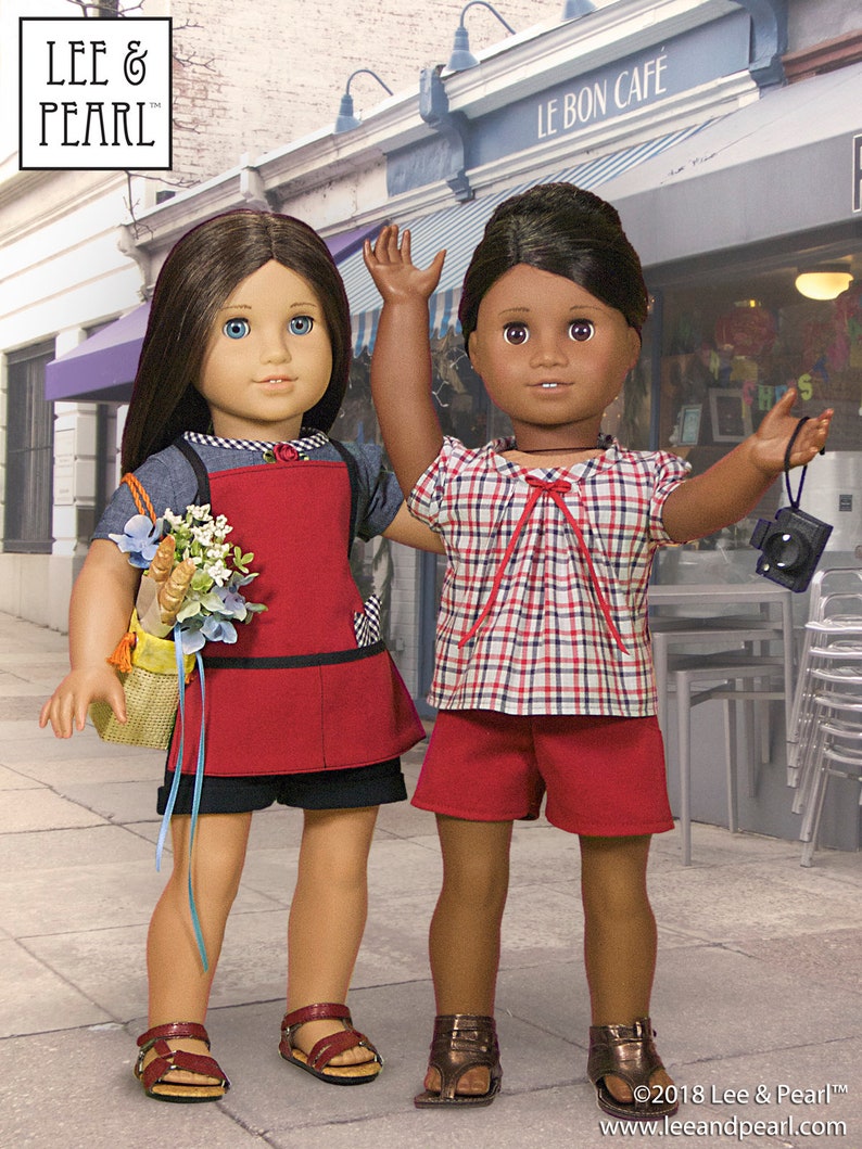 May include: Two dolls, one with brown hair and a red and white plaid shirt and red shorts, and the other with brown hair and a red apron over a blue and white striped shirt, standing in front of a cafe called "Le Bon Cafe".