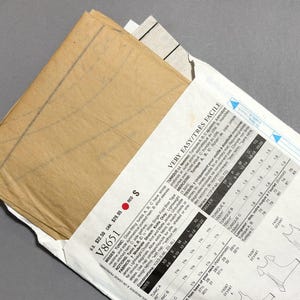 May include: A sewing pattern packet with a tan paper pattern peeking out. The packet is white with black text and diagrams, including the words "VERY EASY/TR&Egrave;S FACILE" and "V8651". The pattern is for a tunic.