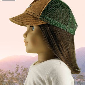 Peut inclure: Un chapeau de camionneur brun et vert avec un dos en maille. Le chapeau est con&ccedil;u pour les poup&eacute;es de 45 cm. Le chapeau a une visi&egrave;re brune et un dos en maille verte. Le chapeau est pos&eacute; sur la t&ecirc;te d'une poup&eacute;e. La poup&eacute;e regarde de c&ocirc;t&eacute;. L'arri&egrave;re-plan est une image floue d'un coucher de soleil.