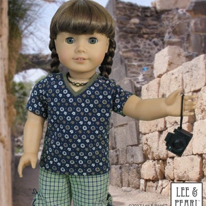 May include: A doll wearing a blue and white floral print short-sleeved shirt and green plaid shorts. The doll is holding a brown and black camera with a strap.