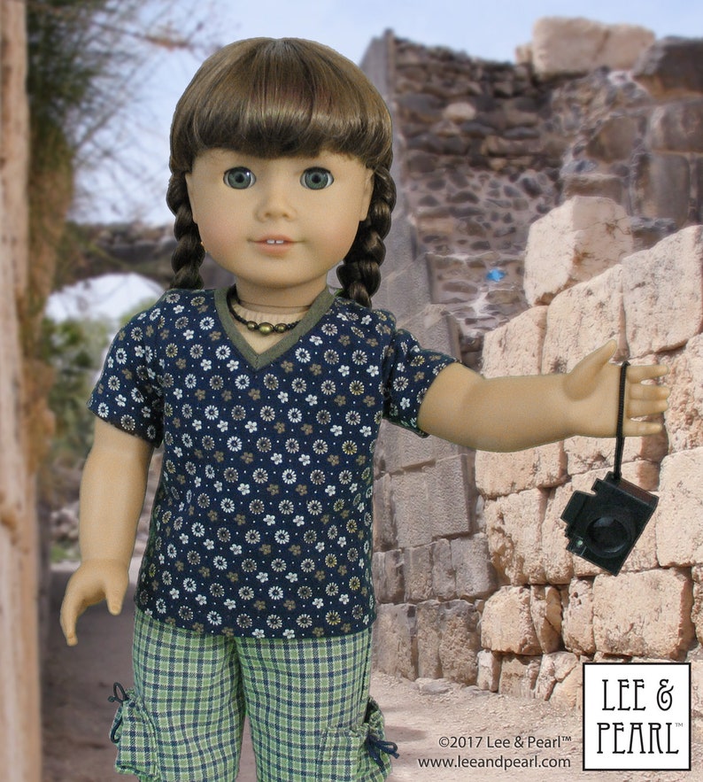 May include: A doll wearing a blue and white floral print short-sleeved shirt and green plaid shorts. The doll is holding a brown and black camera with a strap.