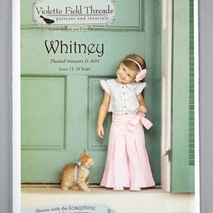 May include: A sewing pattern for a girl's pleated trousers and skirt called "Whitney" by Violette Field Threads. The pattern is shown with a young girl wearing the finished garment and a kitten.