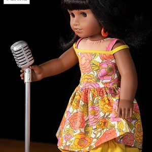 May include: A doll wearing a floral dress with a yellow underskirt and red earrings holds a silver microphone on a stand. The doll has dark hair and brown eyes. The background is black.
