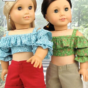 May include: Two dolls wearing off-the-shoulder tops and shorts. The doll on the left is wearing a light blue top with a floral pattern and red shorts. The doll on the right is wearing a green top with a floral pattern and khaki shorts. Both dolls have brown hair and are wearing earrings.