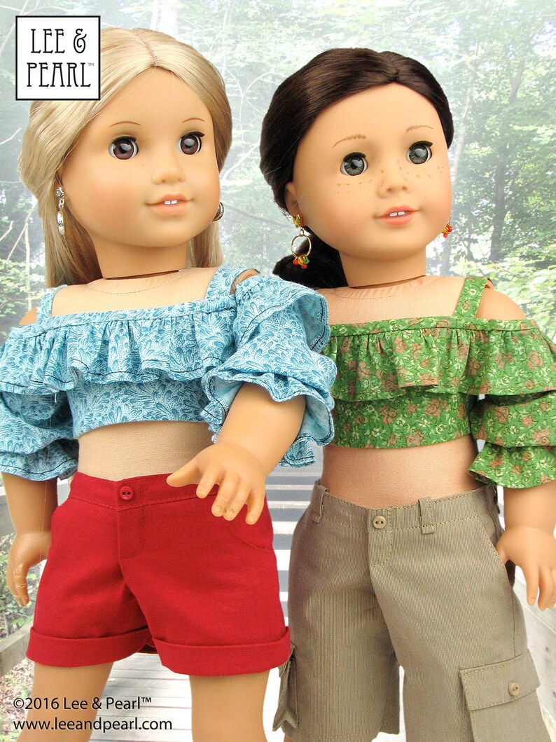 May include: Two dolls wearing off-the-shoulder tops and shorts. The doll on the left is wearing a light blue top with a floral pattern and red shorts. The doll on the right is wearing a green top with a floral pattern and khaki shorts. Both dolls have brown hair and are wearing earrings.