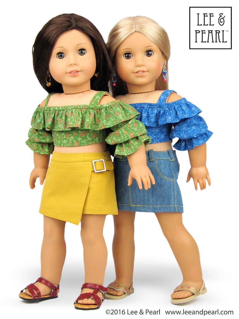 May include: Two dolls wearing off-the-shoulder tops and skirts. The doll on the left is wearing a green floral top and a yellow skirt. The doll on the right is wearing a blue floral top and a blue denim skirt. Both dolls are wearing sandals.