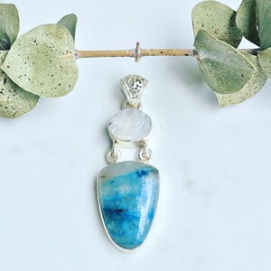 May include: A silver pendant with a blue and white gemstone. The pendant is made of sterling silver and features a delicate design. The gemstone is a beautiful blue color with white streaks.