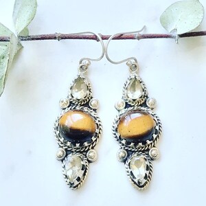 May include: A pair of silver dangle earrings with tiger's eye and clear quartz stones. The earrings have a teardrop shape and are accented with silver beads.