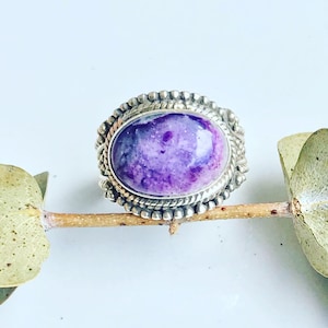 Può includere: Un anello d'argento con una pietra ovale di colore viola e bianco incastonata in una montatura a perline.
